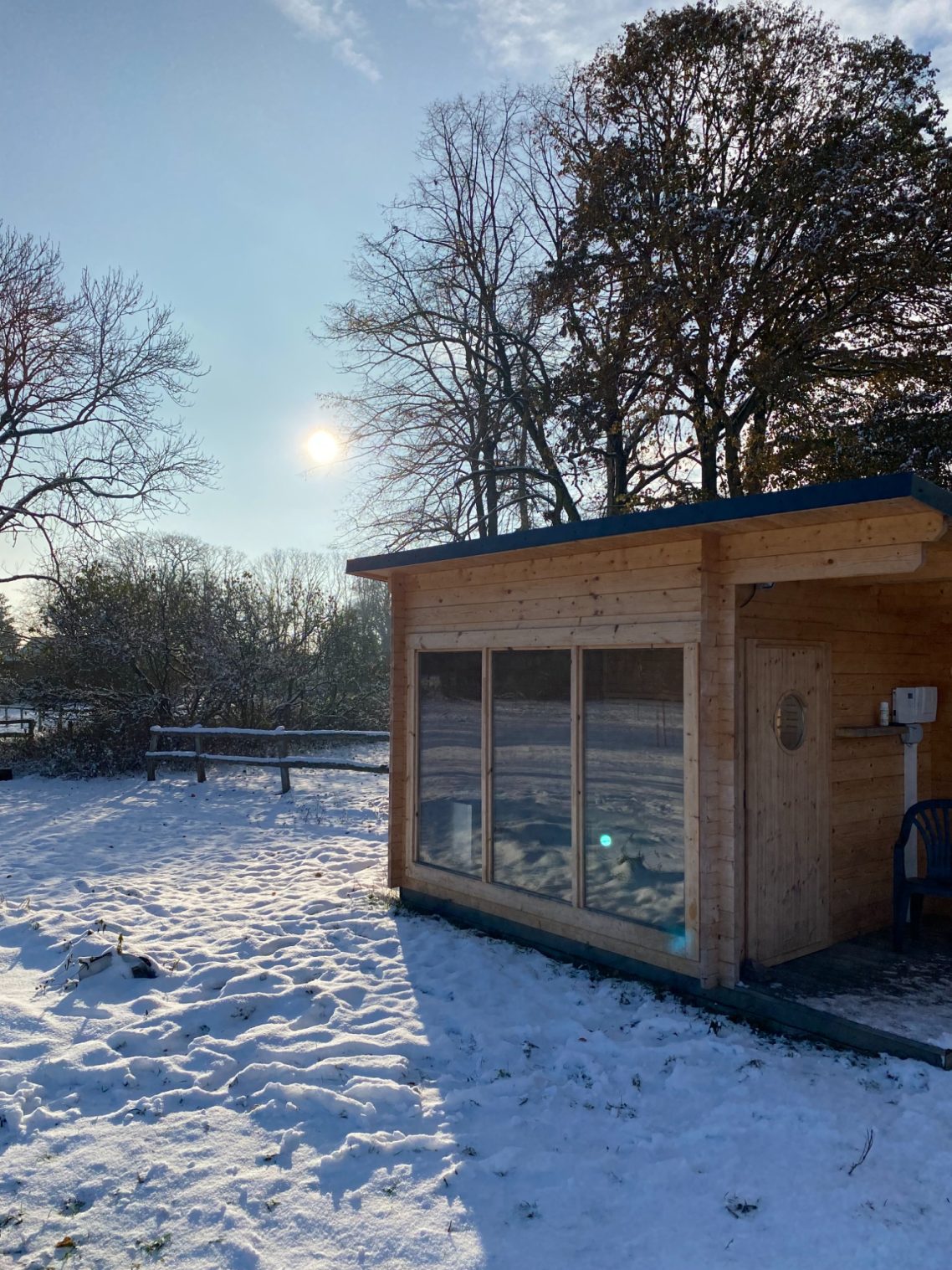 Holzhaus im Schnee mit Sonnenschein und Bäumen im Hintergrund.